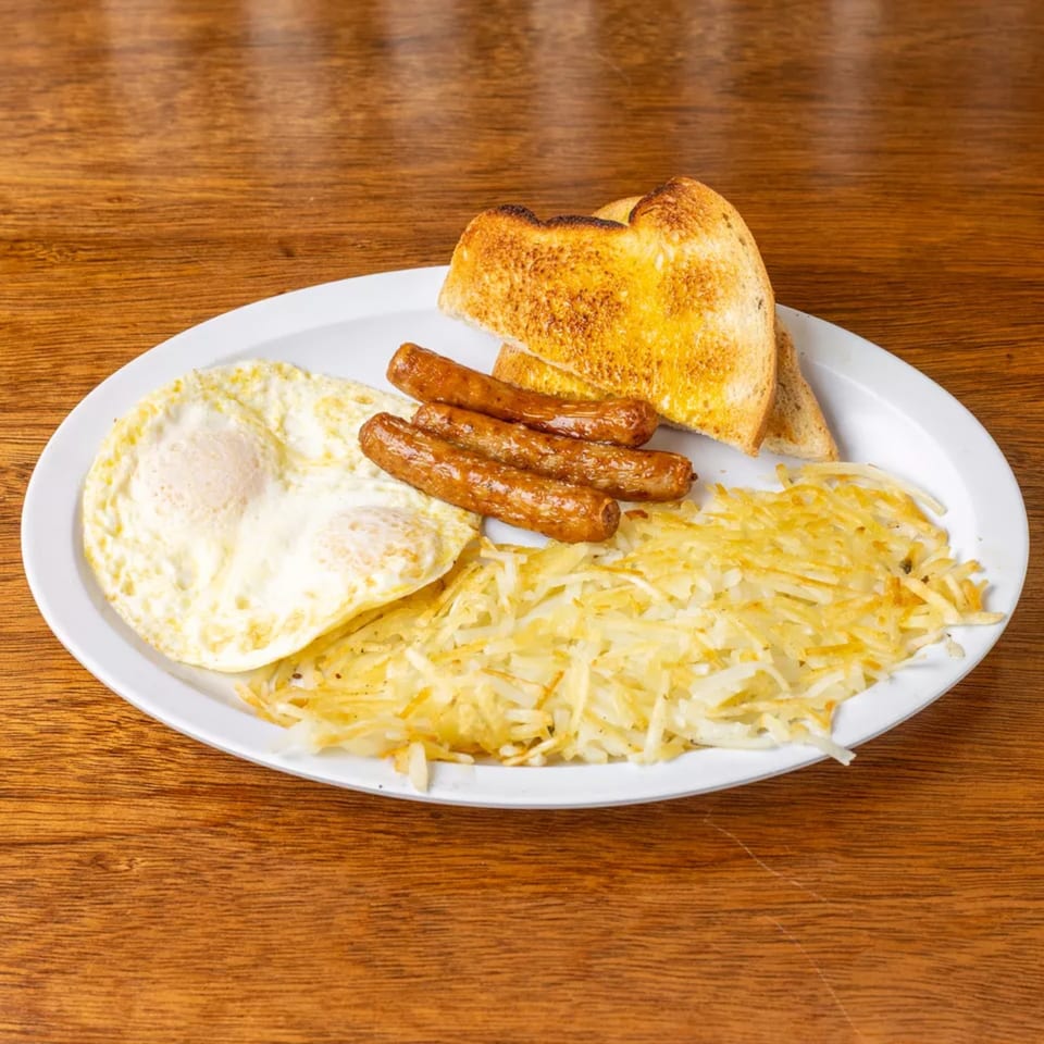 A breakfast platter with fried eggs, sausage links, hash browns, and toasted bread on a white plate.