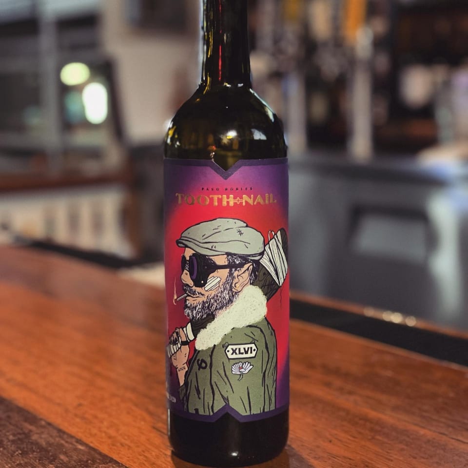 A bottle of Tooth+Nail beer with a cartoon label of a man smoking, on a wooden bar.