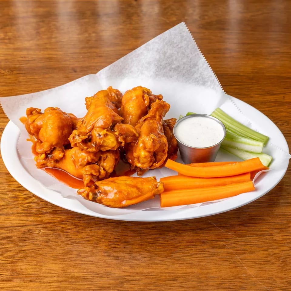 Plate of buffalo chicken wings with ranch dipping sauce, celery, and carrot sticks.