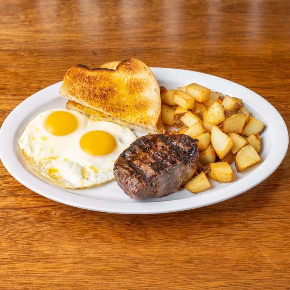 A breakfast plate with grilled steak, two fried eggs, golden hash browns, and toasted bread.