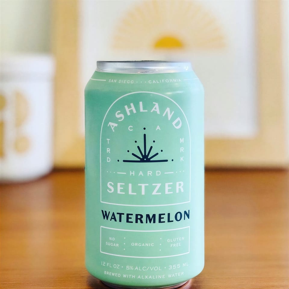 A light green can of Ashland Hard Seltzer Watermelon, with white text, on a wooden surface.