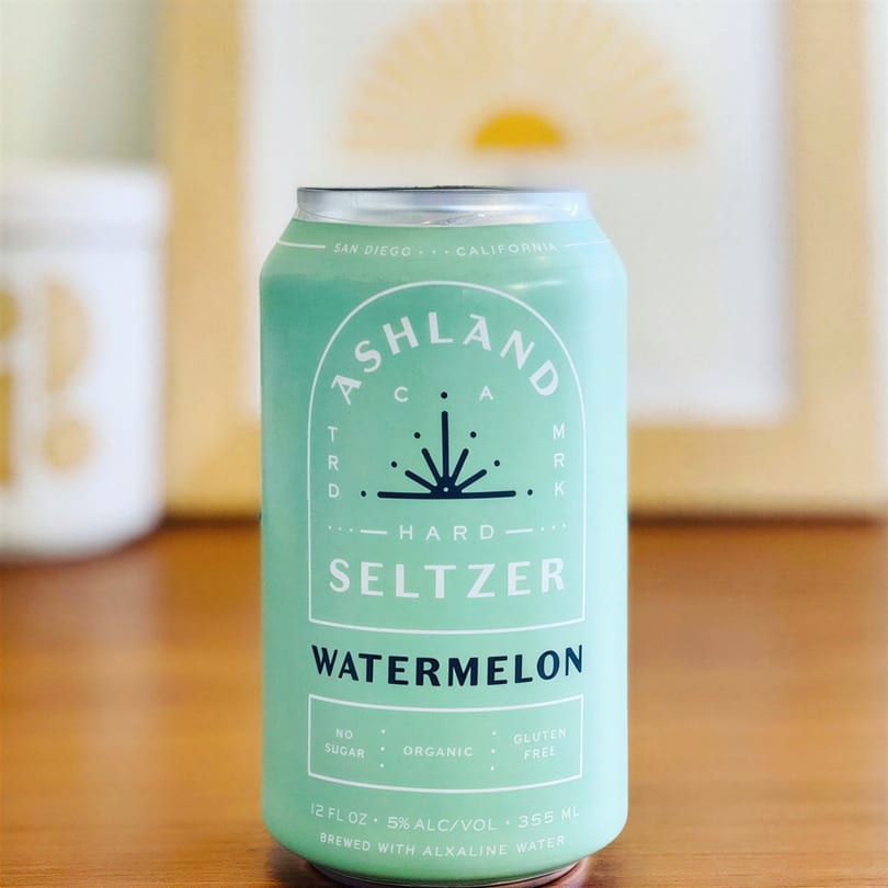A light green can of Ashland Hard Seltzer Watermelon, with white text, on a wooden surface.