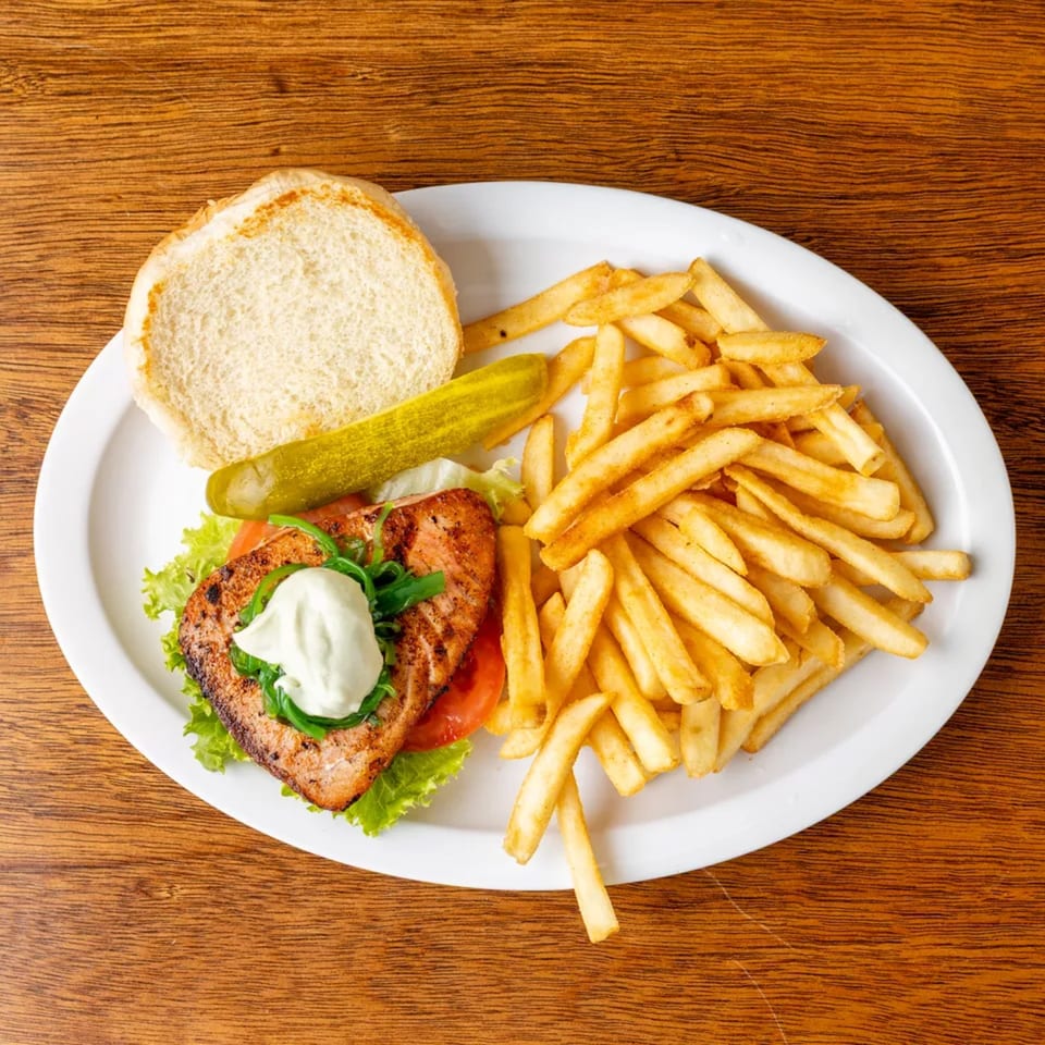 Grilled salmon sandwich with lettuce, tomato, and sauce, served with french fries and a pickle.