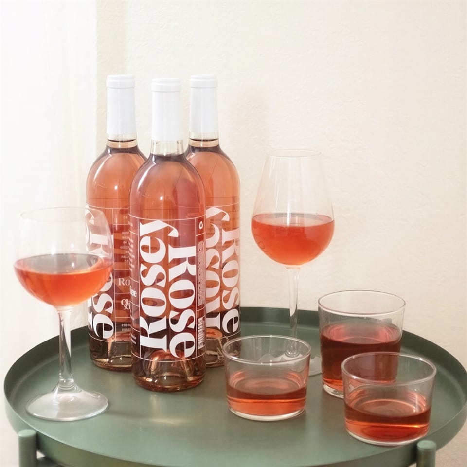 Three bottles of Rosey Rosé wine and several glasses filled with rosé on a green tray.