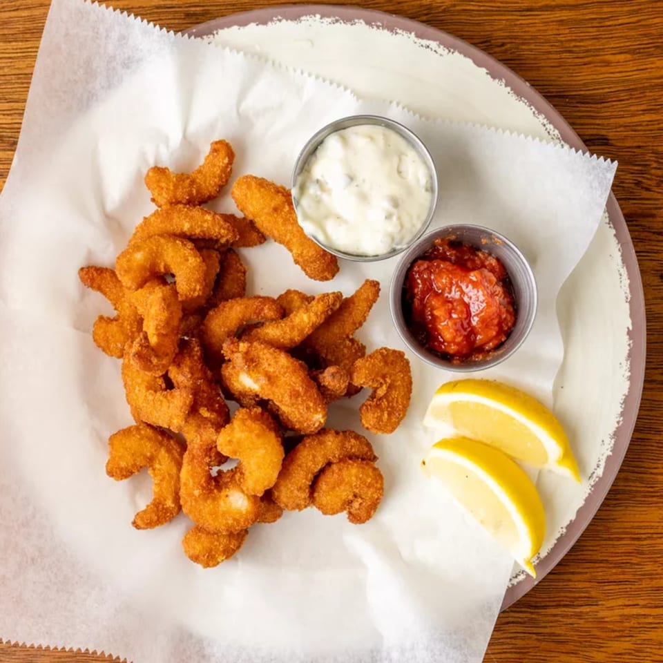 Crispy fried shrimp with two dipping sauces and lemon wedges on a white paper-lined plate.