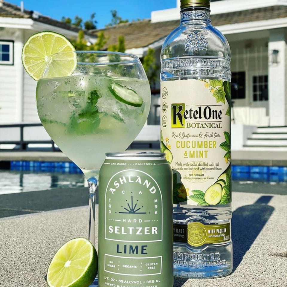A Ketel One Cucumber & Mint bottle, Ashland Lime Seltzer can, and cocktail with lime by a pool.