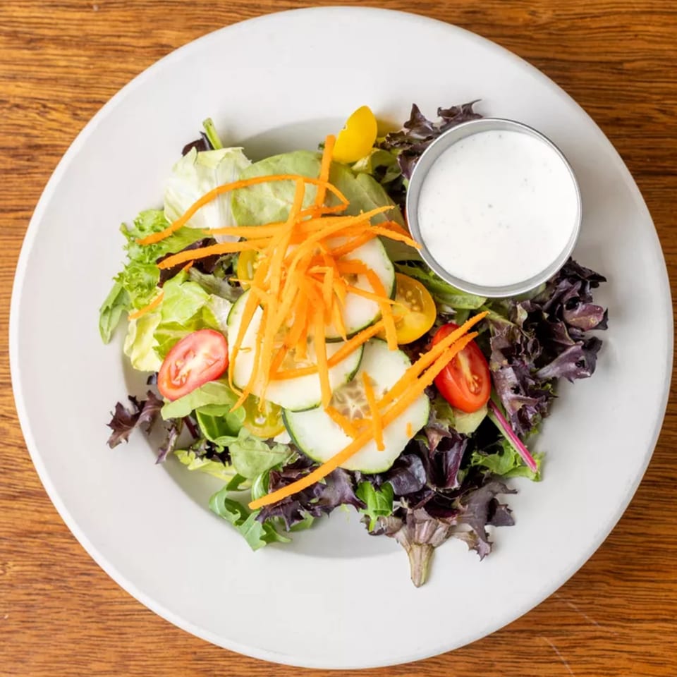 Fresh garden salad with mixed greens, shredded carrots, cucumber, tomatoes, and a side of ranch dressing.