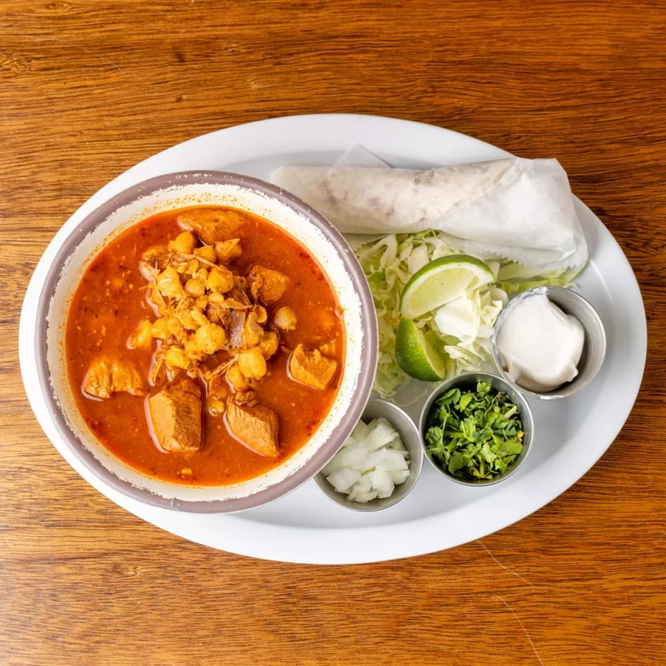 Pozole soup with pork and hominy, served with a burrito, cabbage, lime, onions, cilantro, and sour cream.